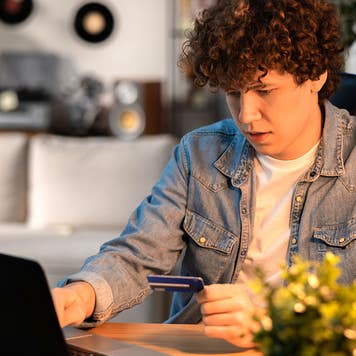 a young man at home holding a credit card and using a computer