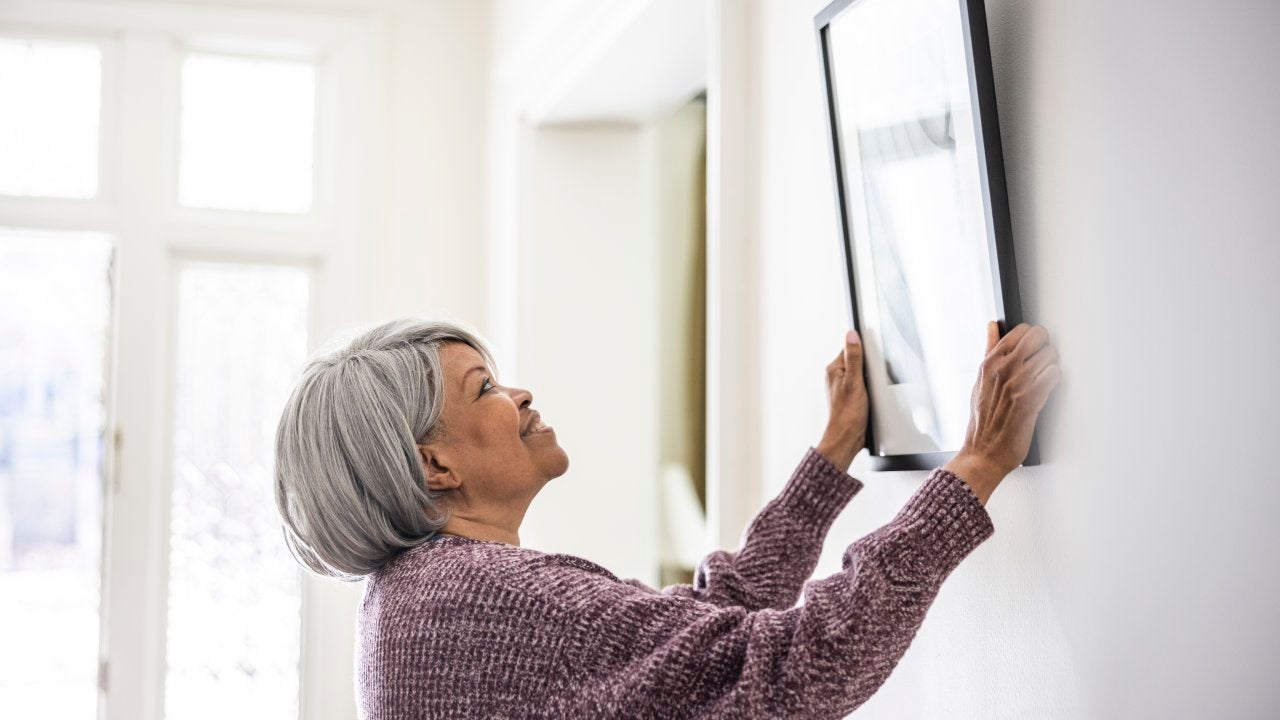 Senior woman hanging picture at home